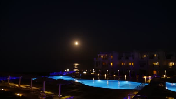 Lapso de tempo. pôr-do-sol sobre o mar. Lua erguida. vista do quarto do hotel para o complexo hoteleiro e sua grande piscina, à noite. país tropical. — Vídeo de Stock