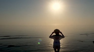 Denizin üzerinde şafak. Denizin üzerinde güneşin doğuşuna hayran olan genç bir kadının silueti. Yaz sabahı.