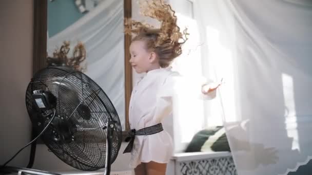 Hair fluttering in the wind. cute little girl is having fun. She stands in front of the fan, the air flows her curly hair, as if in the wind — стоковое видео