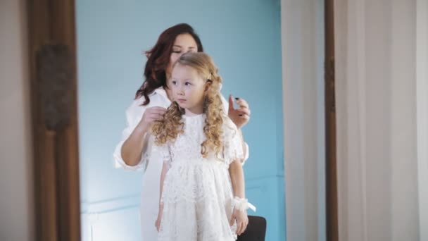 Comb child hair. mom is combing her little daughters hair, doing her hair. woman and little girl stand in front of the mirror. — Vídeo de Stock