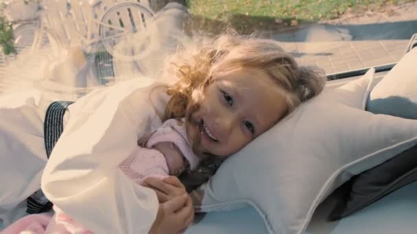 Дитина спить. мила маленька дівчинка. красива маленька принцеса, в обіймах з лялькою, лежить на подушці біля вікна. сонячний день . — стокове відео