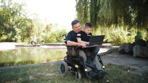 Día de los padres. Papá e hijo. Papá y su hijo pasan tiempo juntos, divirtiéndose. persona con una discapacidad. personas con necesidades especiales. usuario de silla de ruedas. — Vídeo de stock