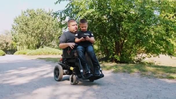 Dzień ojców. Tata i syn. Tata i synek spędzają razem czas, dobrze się bawią. osoba niepełnosprawna. ludzi ze specjalnymi potrzebami. użytkownik wózka inwalidzkiego. — Wideo stockowe