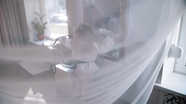 Hair fluttering in the wind. cute little girl is having fun. She stands in front of the fan, the air flows her curly hair, as if in the wind. view through the curtain — Vídeo de Stock