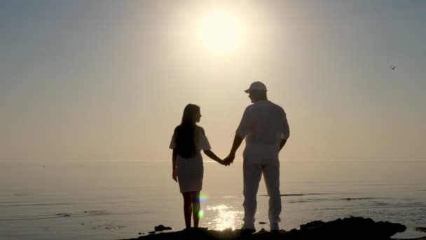Світанок над морем. пара силуетів людей, тато і дочка захоплюються схід сонця над морем. Літній ранок . — стокове відео