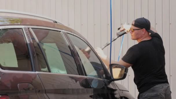 Muž myje auto čistou vodou, vysokotlakým sprejem, venku, v samoobslužné myčce aut. Čištění aut. — Stock video