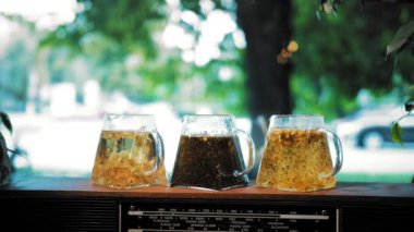 Çaydanlıkta bitki çayı. Çay içeceğim. Yakın plan. Farklı bitkisel renklerde çay ile üç bardak çaydanlık. Yapraklı çiçek, ezilmiş nane, limon, ıhlamur ve papatya çayı..