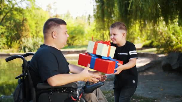 Día de los padres. pequeño niño lindo le da regalos a su padre. un hombre es una persona con discapacidad. usuario de silla de ruedas. personas con necesidades especiales. — Vídeos de Stock