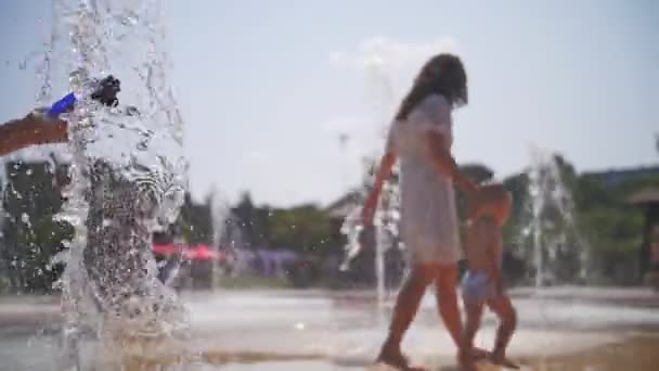 市の噴水。接近中だ。噴水ジェットだ。背景には夏の暑い日に小川や公園の噴水ジェットを楽しむ子供たちが. — ストック動画