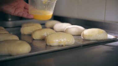 Yemek pişirmek. Fırın. Hamur tatlısı yapmak. Yakın plan. Çiğ hamur hamurlu turtalar, metal bir fırın tepsisine serilmiş, fırında pişirilmeye hazır. Turtalar yumurta sarısı ile kaplanmış.