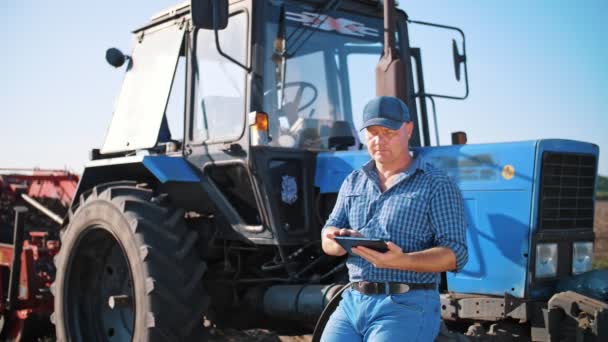 Contadino sta usando tablet digitale. sul campo agricolo, vicino al trattore, sullo sfondo delle macchine agricole. agricoltura intelligente. tecnologie agricole — Video Stock
