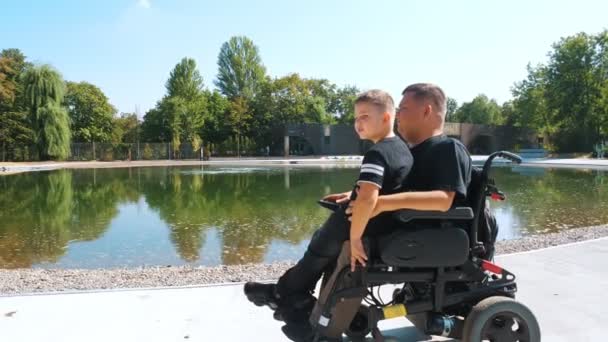 Pappadagen. person med fysisk funktionsnedsättning. Pappa och hans söta son går i parken på sommardagen. Pappa använder rullstol. personer med särskilda behov. — Stockvideo