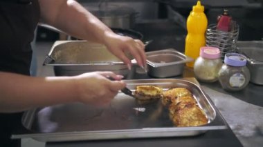 Patates kızartması. Patates köftesi. Yemek pişirmek. Patates keki, zuela. Açık büfe restoran mutfağı. Yakın plan. Aşçı, kızarmış patatesli kekleri metal tepsiye koyar..