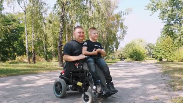 Pappadagen. person med funktionshinder. Pappa och hans söta son går i parken på sommardagen. Pappa använder rullstol. personer med särskilda behov. — Stockvideo
