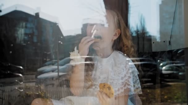 Theekransje. portret. Moeder en dochtertje drinken thee met koekjes, zittend bij het raam, op een grote vensterbank. Zicht door het raam, van buiten — Stockvideo