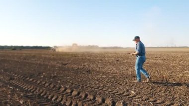 Patates hasadı. Elinde dijital bir tablet tutan çiftçi, tarlada çalışan tarım makineleri ve patates hasatçılarına karşı yeni sürülmüş bir tarlada yürüyor.