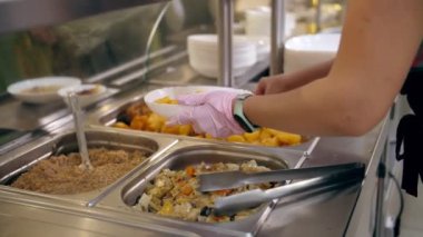 Açık büfe restoranı. Kendi kendine hizmet veren kafeterya. Yakın plan. Garson, koruyucu eldivenlerle, müşteriler için yemek hazırlıyor. Yemek pişirmek. sağlıklı gıda.