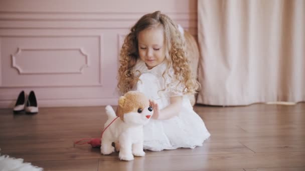 Mignonne petite fille. Chien jouet. petite fille blonde bouclée dans une robe en dentelle blanche joue avec son chien jouet. — Video