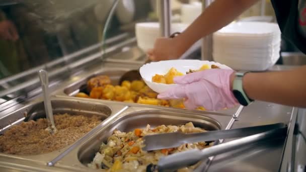 Restaurante buffet. cafetería de autoservicio. Primer plano. camarera, en guantes de protección, pone comida en el plato para el cliente. cocinar. alimentos saludables. — Vídeo de stock