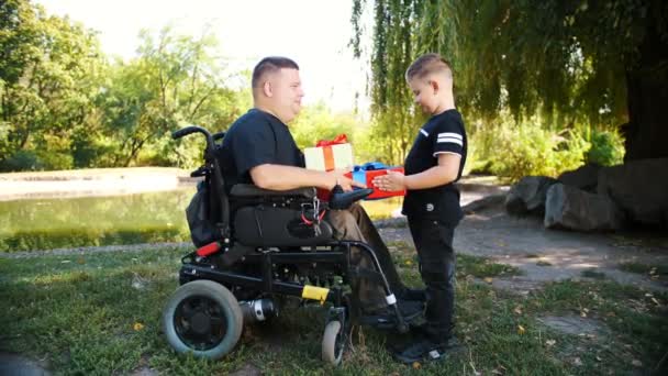 Día de los padres. pequeño niño lindo le da regalos a su padre. un hombre es una persona con discapacidad. usuario de silla de ruedas. personas con necesidades especiales. — Vídeo de stock