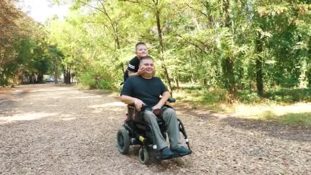 Dia dos pais. pessoa com deficiência. O pai e o seu filho bonitinho vão passear no parque, no dia de verão. O pai é um utilizador de cadeiras de rodas. pessoas com necessidades especiais. — Vídeo de Stock