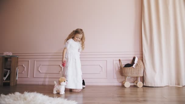 Söt liten flicka. Leksakshund. lockigt blond liten flicka i en vit spets klänning leker med sin leksak hund. — Stockvideo