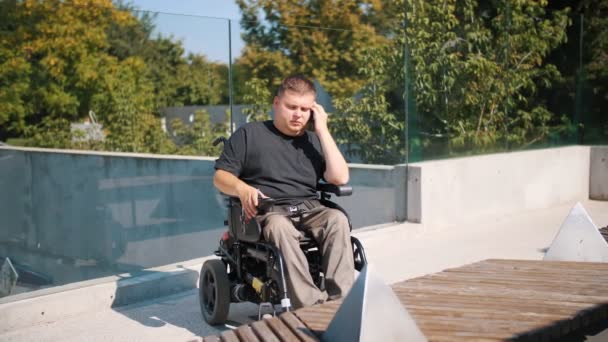 Pessoa com deficiência. um usuário de cadeira de rodas. pessoas com necessidades especiais. O jovem está a falar ao telefone, no parque, no dia de verão. Ele é um usuário de cadeira de rodas. — Vídeo de Stock