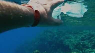 Denizde çöp. Denizi temizle. Denizde tıbbi maske. Sudaki çöpleri toplayın. Yakın plan. Erkek el atıkları yakalar, tıbbi maske kullanır. Birinci şahıs görüşü. Deniz ya da okyanus kirliliği. ortam