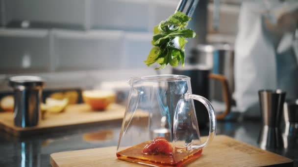 Gyümölcstea elkészítése. Teaital. teát főzök. Közelkép. Friss zöld menta hozzáadása egy üveg teáskanna eper sziruppal. különleges forró gyümölcsteaital főzési folyamata. — Stock videók