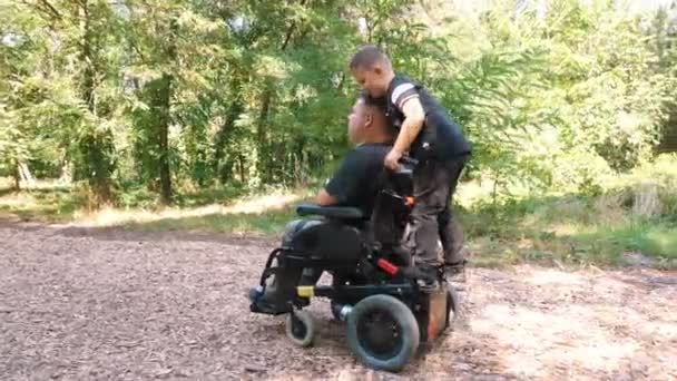 Ημέρα πατέρων. άτομο με αναπηρία. Ο μπαμπάς και ο χαριτωμένος γιος του περπατούν στο πάρκο, την καλοκαιρινή μέρα. Ο μπαμπάς είναι χρήστης αναπηρικής πολυθρόνας. άτομα με ειδικές ανάγκες. — Αρχείο Βίντεο