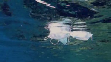 Denizde çöp. Denizde tıbbi maske. Tıbbi maskeler güneş ışığında yavaşça suyun altında sürükleniyorlar. Arka ışıklandırma. Çöp çevresi kirliliği sorunu