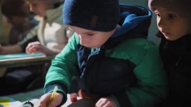 Ukrayna 'da savaş. Sığınak. Çocuklar bodrumda bir sığınakta saklanıyorlar, hava alarmı sırasında, roket ateşi. Çizim yapıyorlar. Rus istilası. Savaşı durdurun. Savaş Yok.