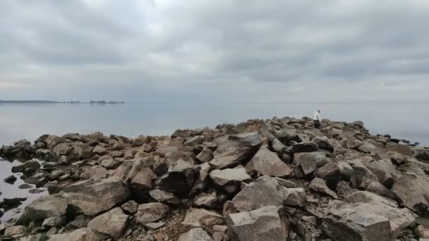 No início da primavera. paisagem. uma adolescente caminha ao longo da costa rochosa perto do rio ou do mar. — Vídeo de Stock