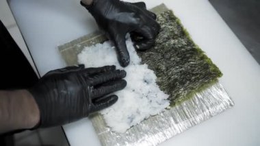 Suşi. Japon yemeği. Yemek pişirmek. Mutfak. Suşi şefi bambu hasırı kullanarak suşi rulosu yapıyor. Norveç yosunlarına pirinç yayıyor. Yakın plan. Restoranın mutfağında..