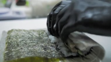 Suşi. Japon yemeği. Yemek pişirmek. Mutfak. Suşi şefi bambu hasırı kullanarak suşi yapıyor. Krem peynirli suşi, salatalık malzemeleri, pirinç, yosun. Yakın plan. Restoranın mutfağında..