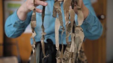 military camouflage net. sewing. Volunteer demonstrates self-made khaki tissue ribbons from shreds of camouflage fabric, for military camouflage nets manufacturing