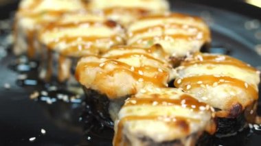 Suşi. Japon yemeği. Yakın plan. Siyah tabakta servis edilen taze pişmiş suşi ruloları dönüyor. Yemek pişirmek. Mutfak. Asya yemekleri.