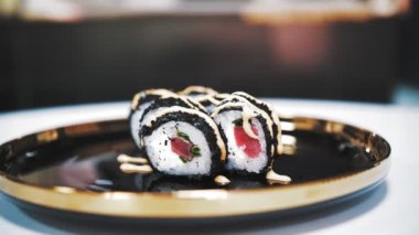 Suşi. Japon yemeği. Yakın plan. Siyah tabakta servis edilen taze pişmiş suşi ruloları dönüyor. Yemek pişirmek. Mutfak. Asya yemekleri.