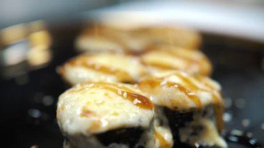 Geleneksel Japon yemekleri. Yakın plan. Suşi şefi susam tohumlarını serpiyor taze pişmiş suşi ruloları, siyah tabakta servis ediliyor. Bir restoranda sanat hizmeti. Asya yemekleri