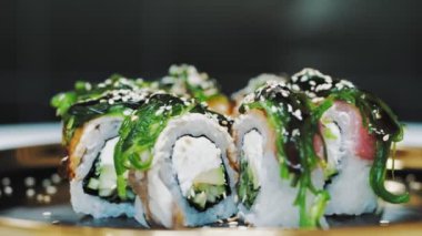 Suşi. Japon yemeği. Yakın plan. Siyah tabakta servis edilen taze pişmiş suşi ruloları dönüyor. Yemek pişirmek. Mutfak. Asya yemekleri.