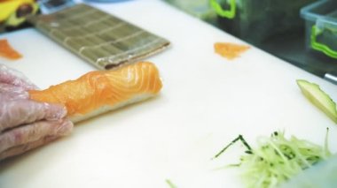 Suşi. Japon yemeği. Yemek pişirmek. Mutfak. Suşi şefi bambu hasırı kullanarak suşi yapıyor. Somonla yuvarlan. Yakın plan. Restoranın mutfağında..