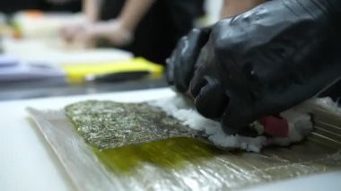 Suşi. Japon yemeği. Yemek pişirmek. Mutfak. Suşi şefi bambu hasırı kullanarak suşi yapıyor. Krem peynirli suşi, salatalık malzemeleri, pirinç, yosun. Yakın plan. Restoranın mutfağında..