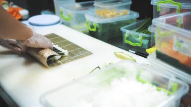 Suşi. Japon yemeği. Yemek pişirmek. Mutfak. Suşi şefi bambu hasırı kullanarak suşi yapıyor. Krem peynirli suşi, salatalık malzemeleri, pirinç, yosun. Yakın plan. Restoranın mutfağında..