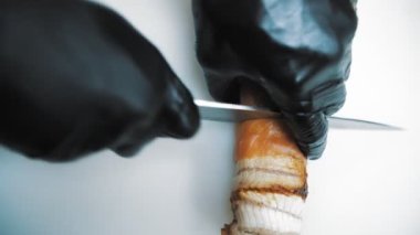 Suşi. Japon yemeği. Yemek pişirmek. Mutfak. Yakın plan. Üst Manzara. Suşi şefi beyaz bir tahtada bıçakla suşi rulosunu küçük parçalara ayırıyor.