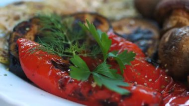 Izgara sebze. Yemek pişirmek. Yakın plan. Döndürme. Izgarada kızartılmış, tabakta barbekü sebzeleri var. Vejetaryen yemeği ve sağlıklı yemek..