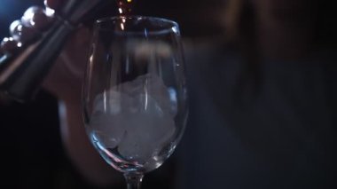 Kokteyl. Kokteyl yapıyorum. Yakın plan. Barmen, barın üstünde buzlu bir şarap bardağına beher kullanarak alkollü içecek doldurur. koyu arkaplan