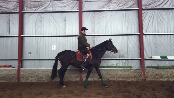 特別な格納庫の黒 サラブレッド馬 乗馬療法に乗る若い男が無効になっているを学習します 彼の右脚ではなく人工的な肢を持っています 障害者のリハビリテーションの概念 — ストック写真