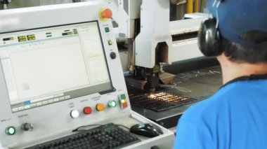 laser metal cutting. close-up. operator supervises operation of laser cutting machine for sheet metal sitting in front of a monitor, computer. laser is cutting patterns on sheet metal plate.