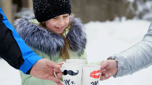 against the background of winter forest, a girl of seven years drinks tea from a cup, on the cups, sponges are drawn. Family tea in the winter forest, winter picnic. High quality photo