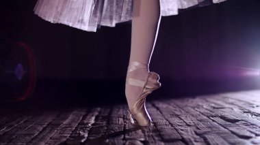 close up, in rays of spotlight, on stage of old theater hall. ballerina in white ballet skirt, rotates on toe in pointe shoe, performs elegantly a certain ballet exercise, tour,pointe. High quality